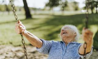 Eine alte Frau lachend auf einer Schaukel.
