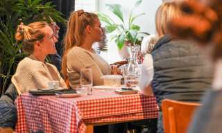 Mehrere Menschen sitzen beim «Wissen zum Zmittag» im Berner Generationenhaus an einem langen Tisch mit rotweiss-kariertem Tischtuch.