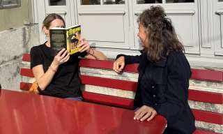 Zwei Personen lesen auf einer Bank ein Buch.