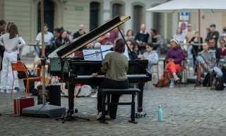 Eine Frau spielt auf einem Klavier und das Publikum ist eingeladen, mitzusingen.