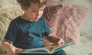 Ein Kind sitzt auf bequemen Kissen und schaut ein Buch an.